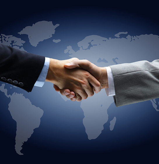 A close-up of two hands shaking over a world map background, symbolizing global business partnerships.